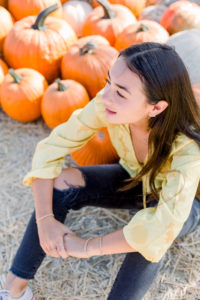 image of woman sitting next to pumpkins at a pumpkin patch