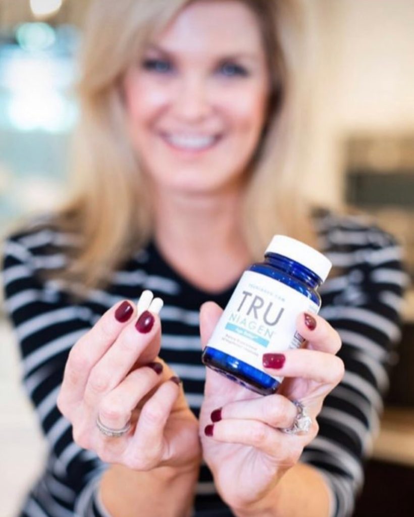 Close up of woman's hands with nutraceutical product, and woman smiling in the background