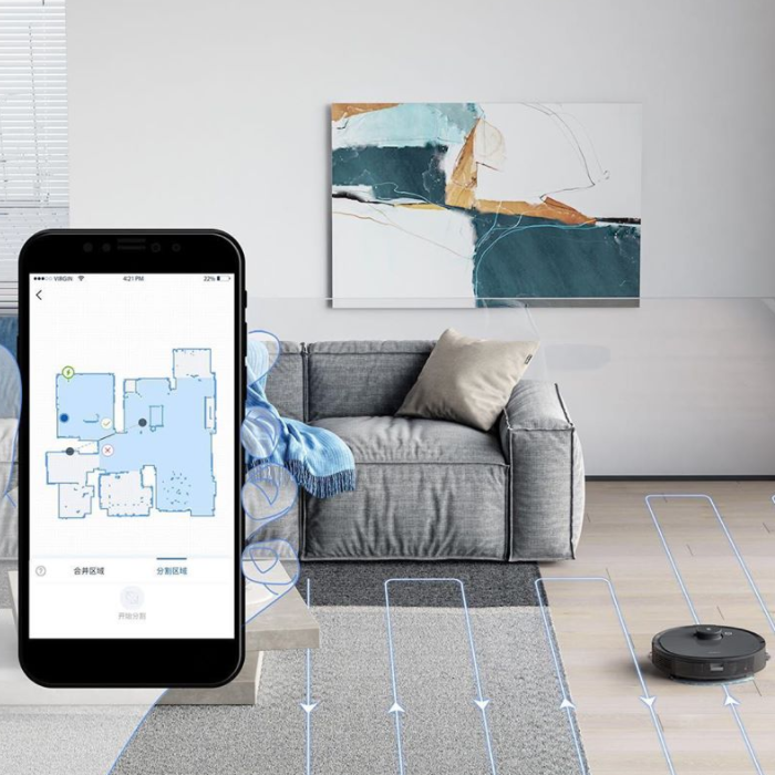 Living room couch with a robot vacuum next to it, with an overlay photo of a cell phone showing a house's blueprint in an app
