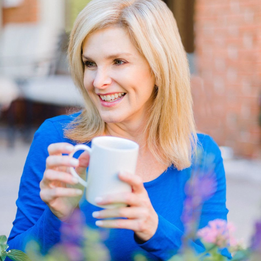 Middle-aged blonde woman smiling with a mug and blue shirt