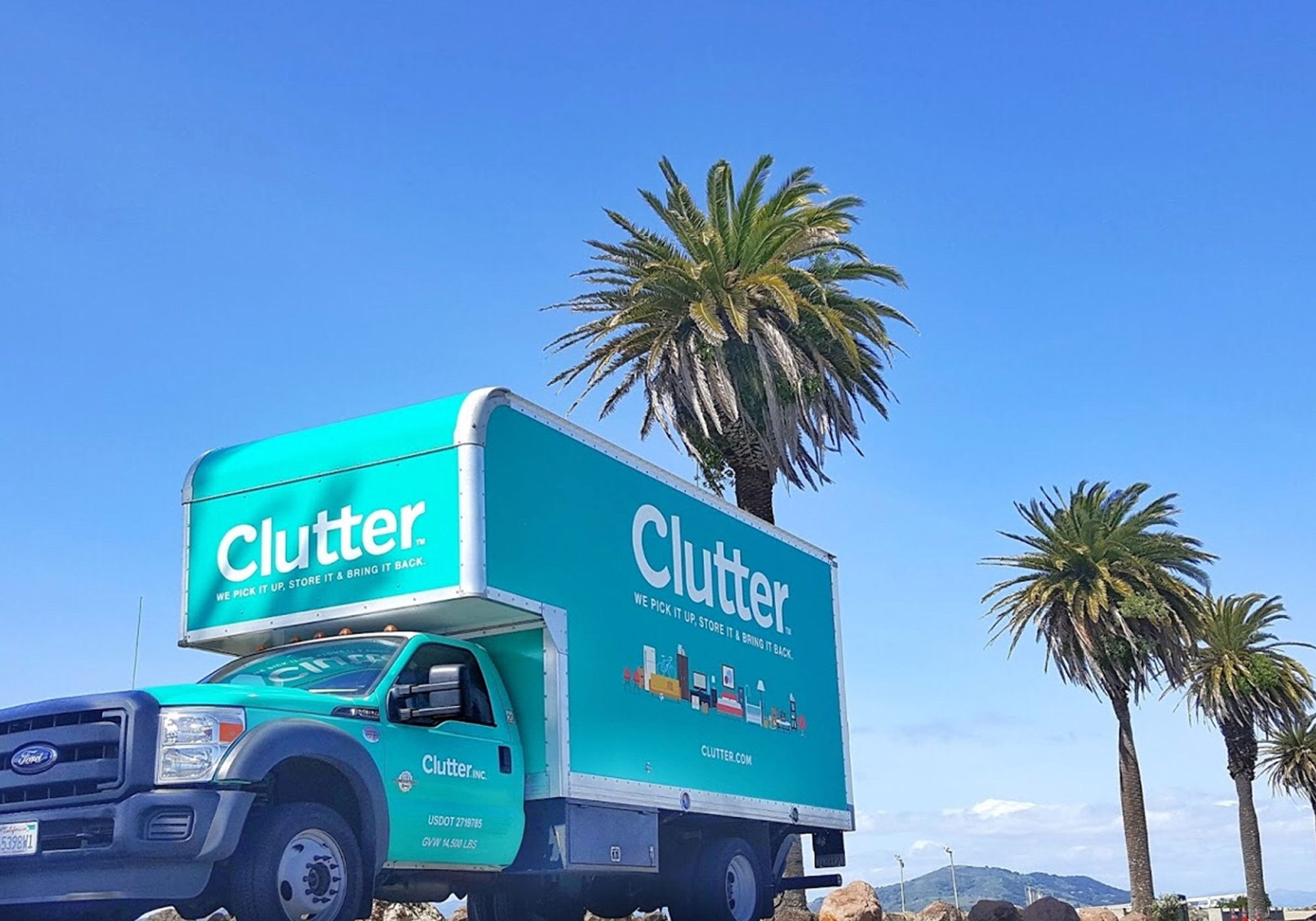 Clutter truck driving through an area with palm trees and mountains in the distance