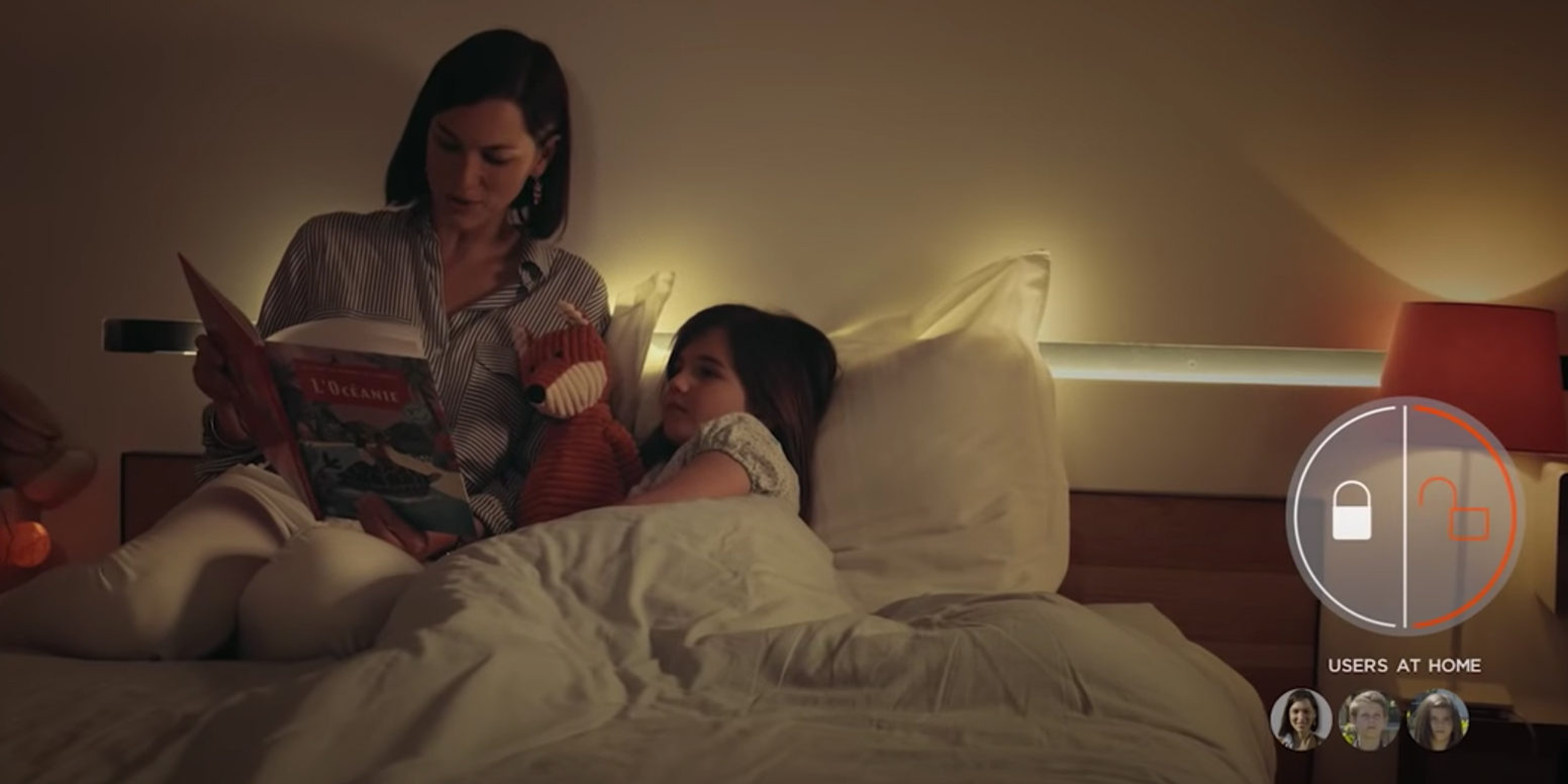 Woman reading a bedtime story to girl who's holding a fox stuffed animal with an overlay of the myfox security app showing who is home