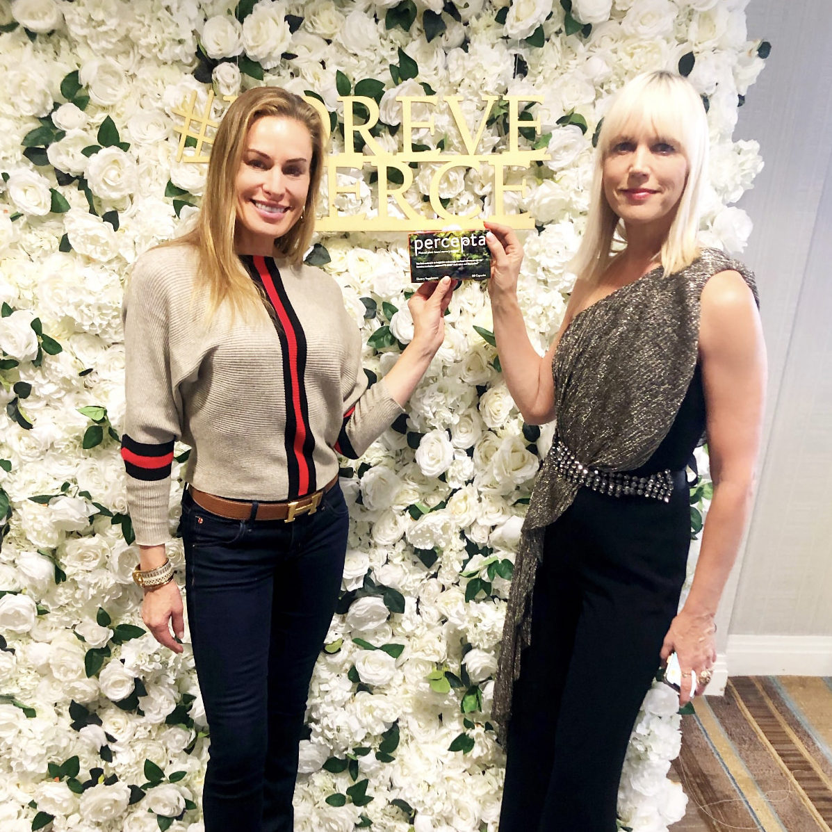 Two women influencers holding a box of percepta standing in front of white rose display