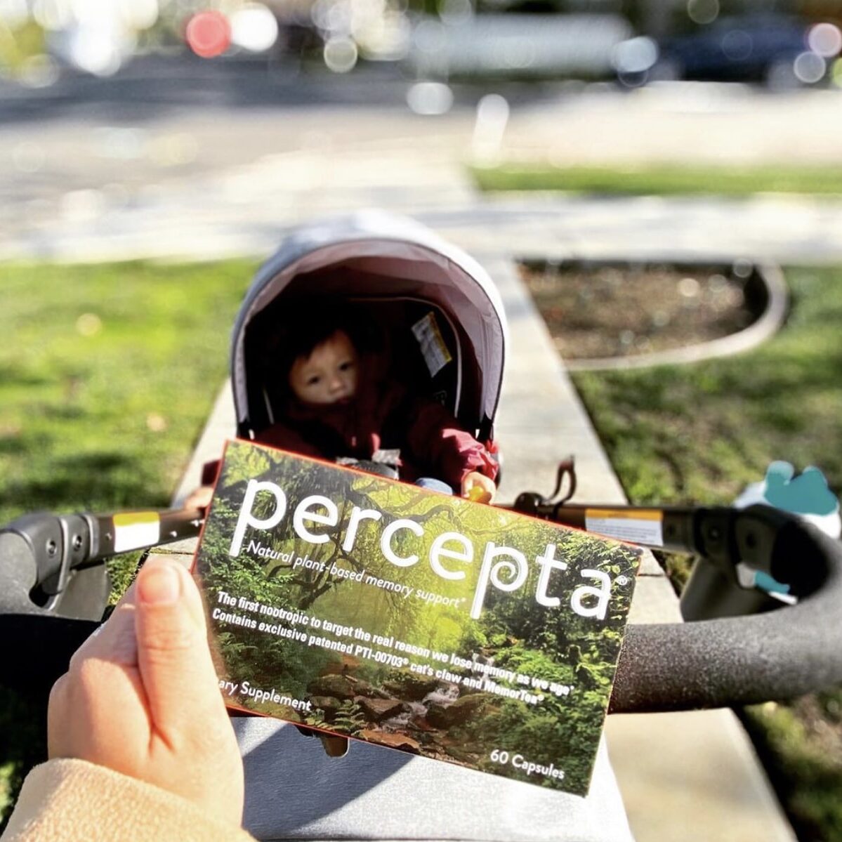 Box of Percepta and a baby in a stroller Person pushing a stroller, holding a box of Percepta with a baby in the stroller in the background